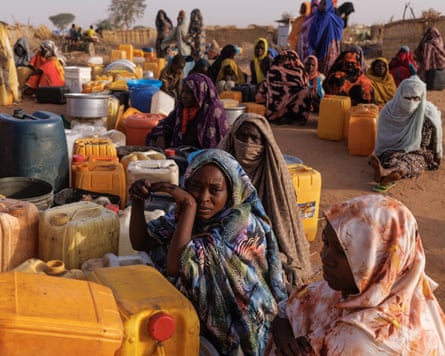 Displaced people sit among large plastic water containers