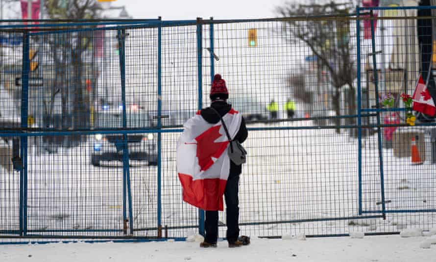 A lone protester stands draped in the Canadian flag at a temporary fence controlling access to streets near parliament in Ottawa.