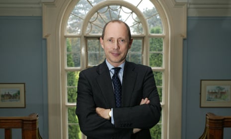 Sir Andrew Dilnot stands with his arms folded, framed by a glass door that looks out on a garden