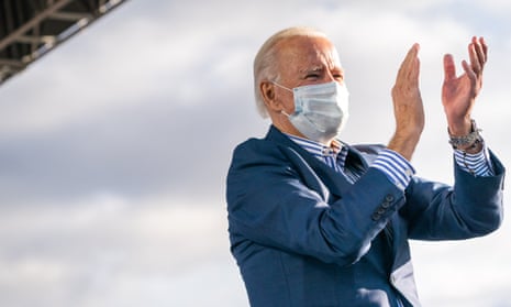 Joe Biden, wearing a mask, claps on stage