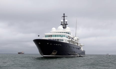 An imposing blue-hulled superyacht with a dark blue hull and white superstructure at sea on a cloudy day
