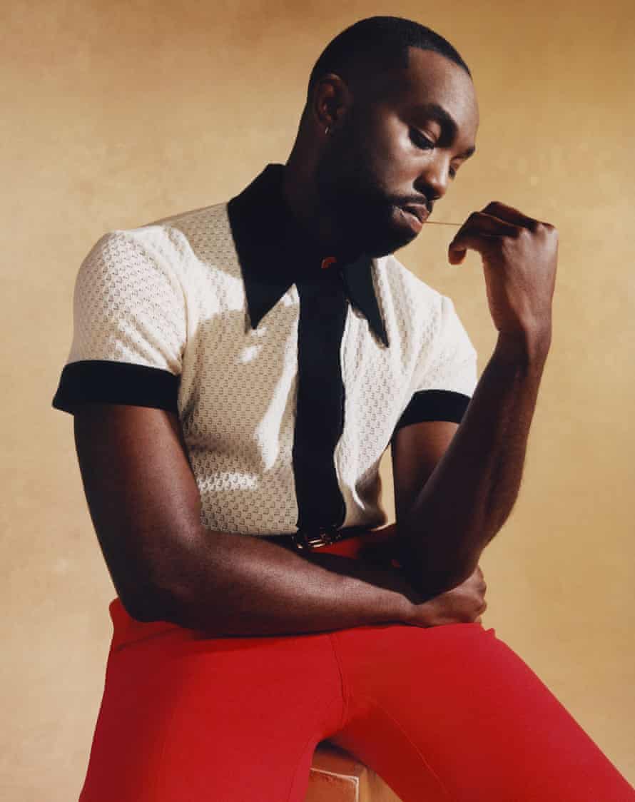 Actor Paapa Essiedu in black and white shirt and red trousers, against beige background