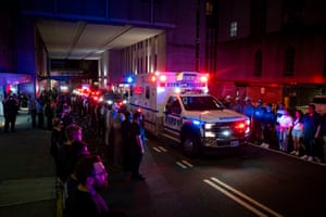 People line a road as an ambulance marked NYPD Police drives by