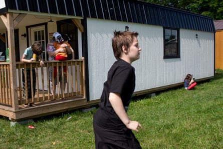 Children play while a woman holds a small child on the porch of a small home.