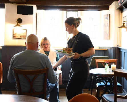 A member of staff brings plates to a couple sitting at a table in the pub
