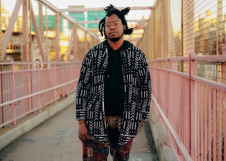 Edward Ongweso Jr wearing a bold patterned black-and-white jacket over a black hoodie, standing on a pedestrian bridge by a highway