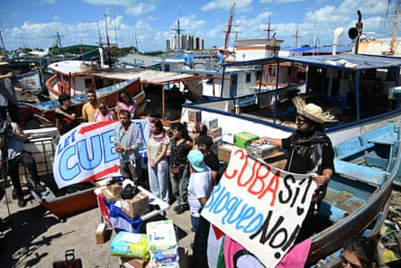 Activists hold a sign reading ‘Cuba Yes! Embargo No!’ in front of a line of boats at a harbourside.