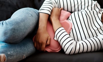 Cropped picture of a woman lying on her side clutching a hot water bottle to her stomach
