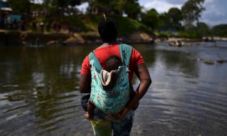 A migrant carrying a baby crosses the Chucunaque River after walking for five days in the Darién Gap.