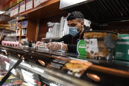 A man wearing gloves and a mask prepares food in a bodega in New York.