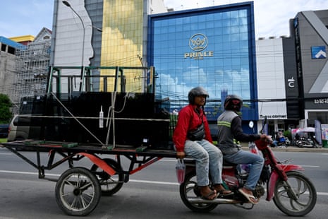 Workers ride a motor-cart loaded with glass past a branch of the Prince Bank