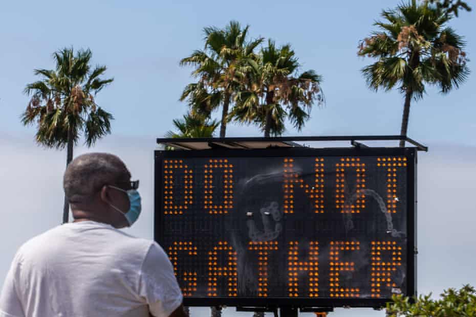 A man wearing a face masks checks his phone near a sign urging people not to gather in Long Beach, California, on 14 July. 