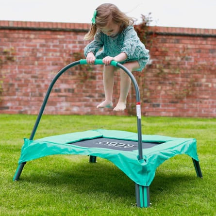 A girl jumps in the air while bouncing on a Rebo Junior toddler trampoline and holding the curved bar
