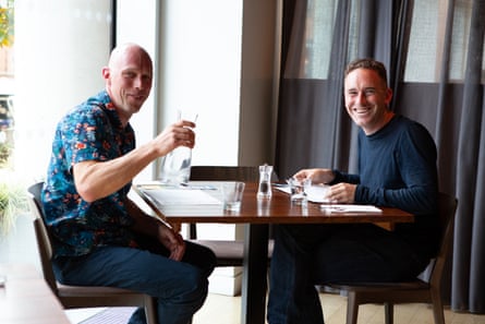 Andrew and Oliver sit at a restaurant table,, smiling at the camera