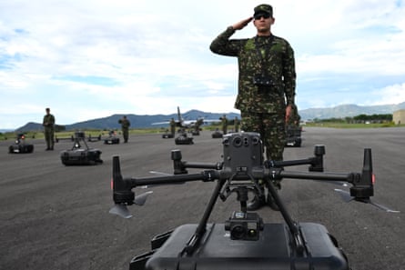 A soldier salutes as he stands in front of a drone on a runway.