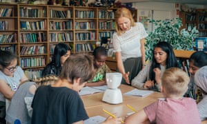 An AV1 robot on a classroom table surrounded by pupils and a teacher