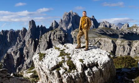 Chris Packham on a boulder in front of a mountain range dressed entirely in varying shades of beige