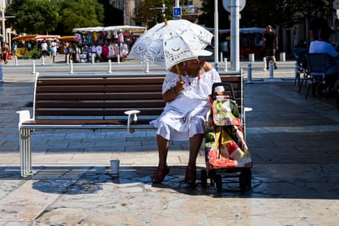 a woman sits under an umbrella on a bench