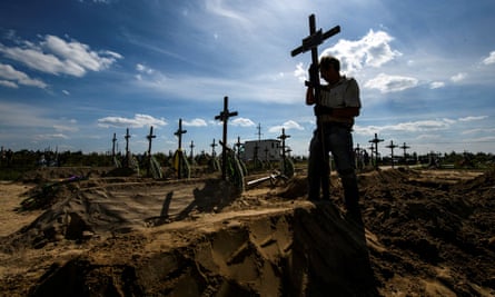 A volunteer places a cross on a grave in Bucha