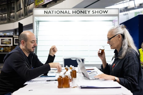 Two people sit opposite each other at a table while inspecting jars of honey