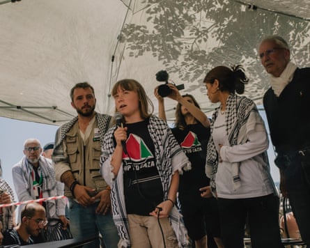Climate activist Greta Thunberg holding a microphone as she gives a speech surrounded by other people.