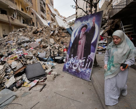 A woman passes next of a poster of Iran’s late supreme leader Ayatollah Ali Khamenei in front of a destroyed building in in Dahiyeh, Beirut’s southern suburbs.