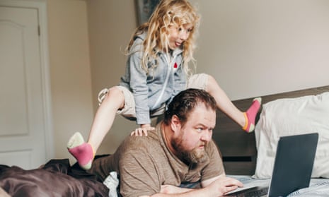 Father working on laptop in bedroom with child daughter on his back