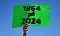 a person holds a neon green sign that reads "1864 does not equal 2024"