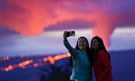 Two women taking a selfie against an erupting volcano