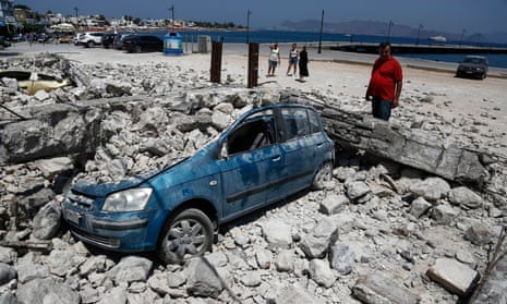 A man looks at a car crushed under rubble near the port in Kos