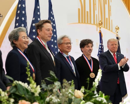 A row of people in suits stand in front of American flags smiling with medals as Donald Trump, standing on the end, claps
