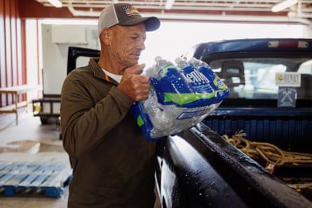 A man in a cap loads a pack of bottled water into his truck.