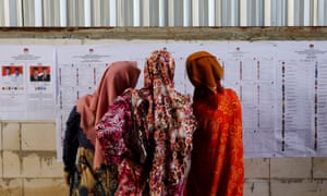 Women look at voting information at a polling station during elections in Bogor, West Java, Indonesia.