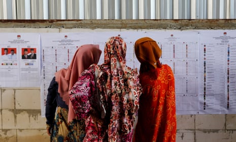 Women look at voting information at a polling station during elections in Bogor, West Java, Indonesia.