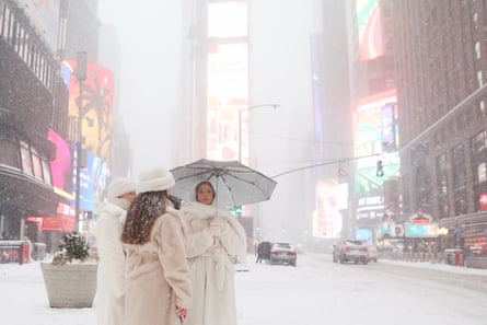 three women wearing fur coats stand on snowy city street