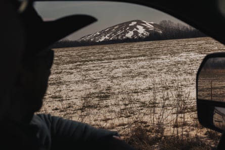 silhouette of a man driving in his truck as he looks out to a giant mound of dirt covered in snow containing toxic chemicals