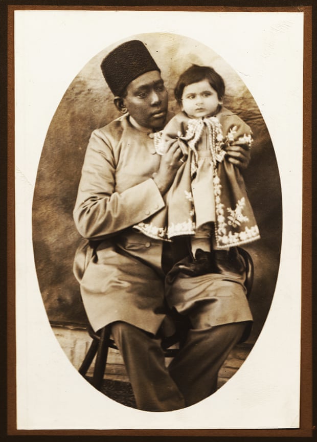 Based on the captions of other photos from the same album written by Masoud Mirza Zell-e-Soltan, the photographer of this image is Zell-e-Soltan himself and the baby in the picture a granddaughter, probably Nim Taj Khanum (Lady Nim Taj), with her African slave, in Isfahan, 1890s. During the Qajar period babysitting and accompanying royal and aristocratic children to their classes were among the main duties of African slaves.