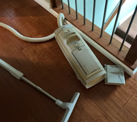A cream-coloured cylinder vacuum cleaner and attachment sit on a wooden floor