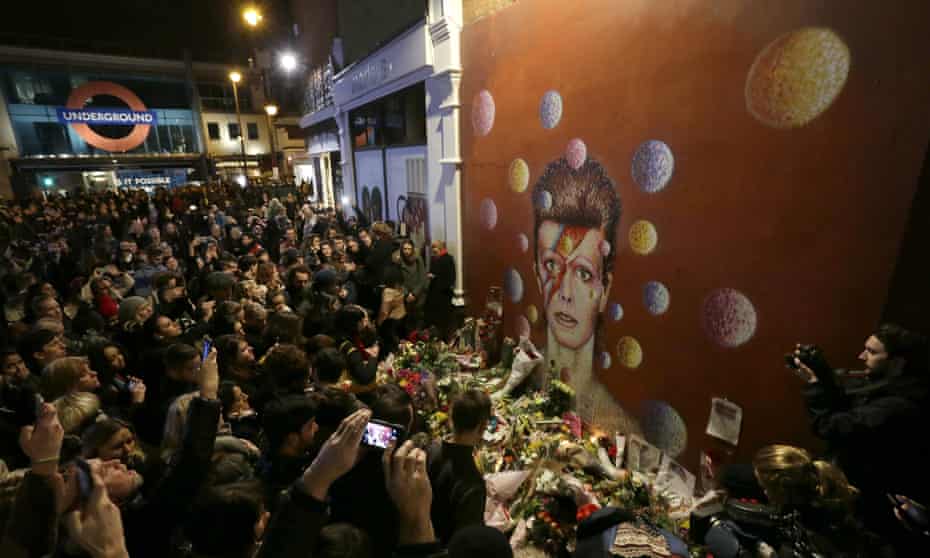 People gather next to tributes left near the mural of David Bowie in Brixton, south London.