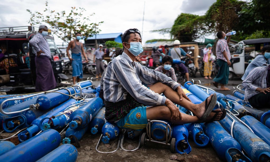 A man sits on empty oxygen canisters, as he waits to fill them up, outside a factory in Mandalay amid a surge in Covid-19 coronavirus cases in Myanmar