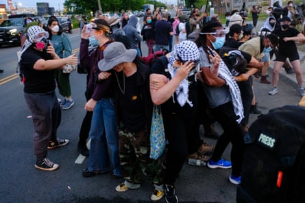 a group of people with linked arms walk backward after being sprayed with a chemical irritant