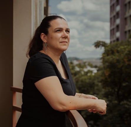 A dark-haired woman with her hair pulled back in a pony tail, wearing a black T-shirt and standing on a balcony