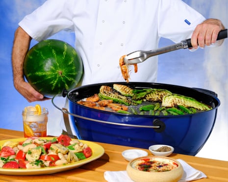 Studio shot of a chef (torso and arms only shown) cooking prawns and courgettes on a blue barbecueCharcoal Barbecue courtesy of Weber.