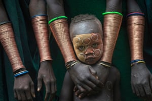 A boy with painted face among women's forearms covered in the copper bracelets