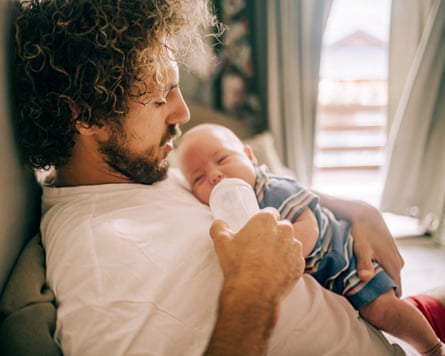 A father on the sofa gives a tiny baby a bottle