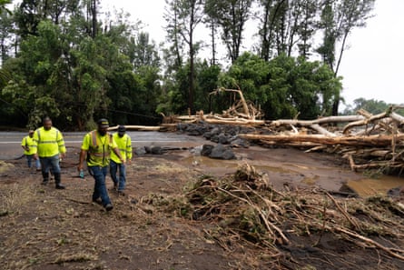 people in reflective clothing walk along a damaged road