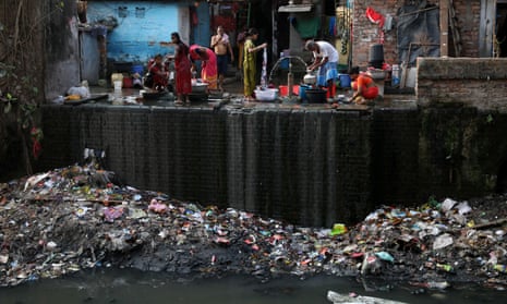 People fill water containers and wash their clothes from municipal water pipes alongside a polluted water channel in Kolkata, India