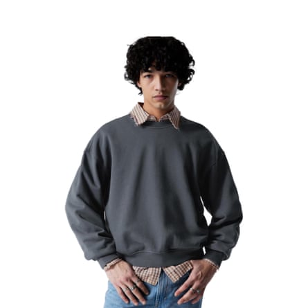A model wears a checked shirt under a boxy grey sweatshirt.
