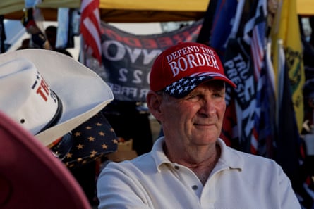 A middle-aged man in a “Defend the border” cap surrounded by rightwing merchandise.