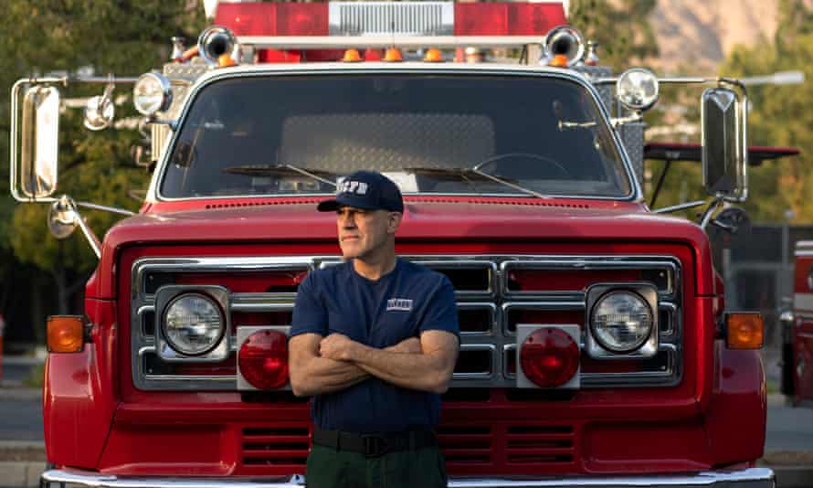 man standing with arms crossed across his body standing in front of firetruck